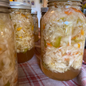 Jars of canned coleslaw sitting on a red and white plaid cloth.