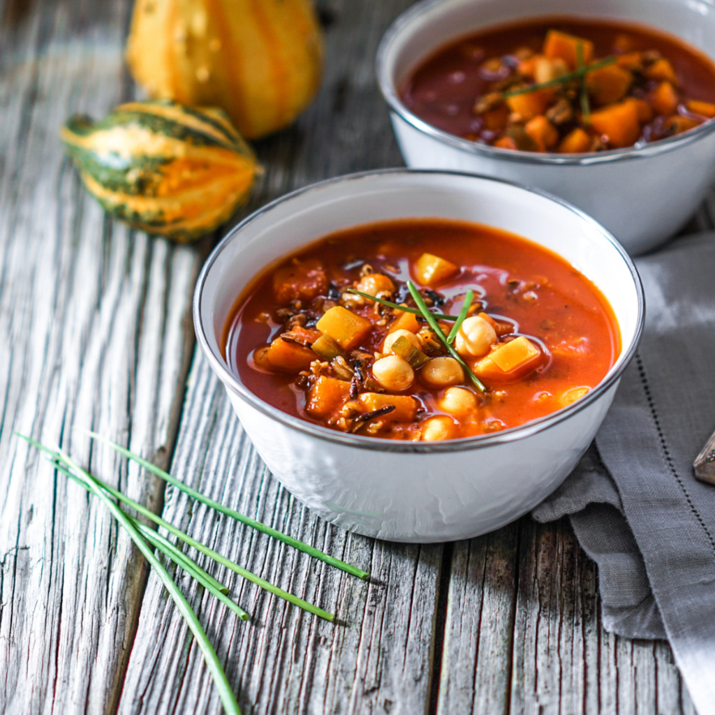 White bowls filled with chili, sitting next to gourds.