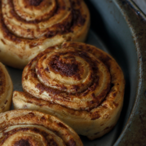 A dark grey metal pan with freshly baked but not frosted cinnamon rolls.