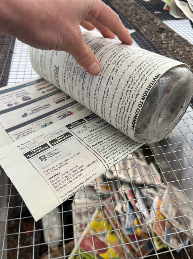 A hand rolling newspaper around a mason jar.