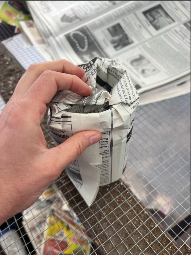 A hand folding the newspaper over the bottom of a mason jar.