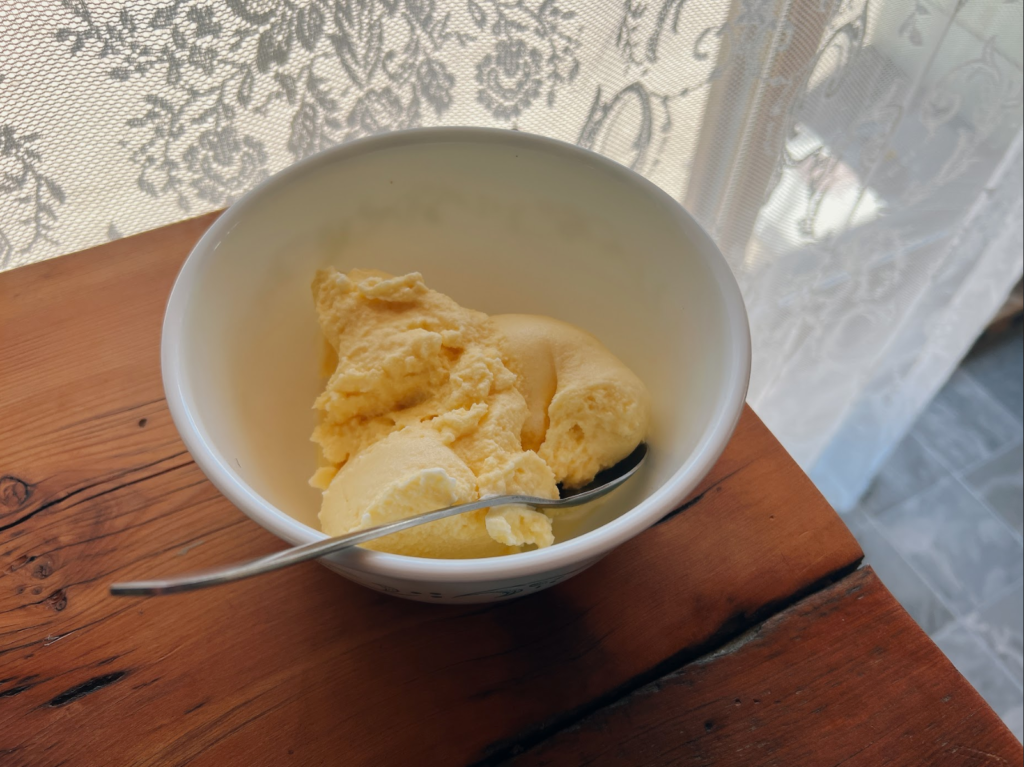 A white bowl with homemade rich and creamy french vanilla ice cream in it and a spoon on a wooden counter.