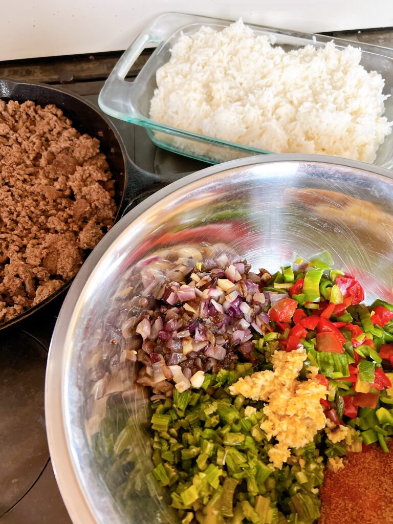 A stainless steel bowl with chopped onions, peppers, tomatoes and other vegetables.