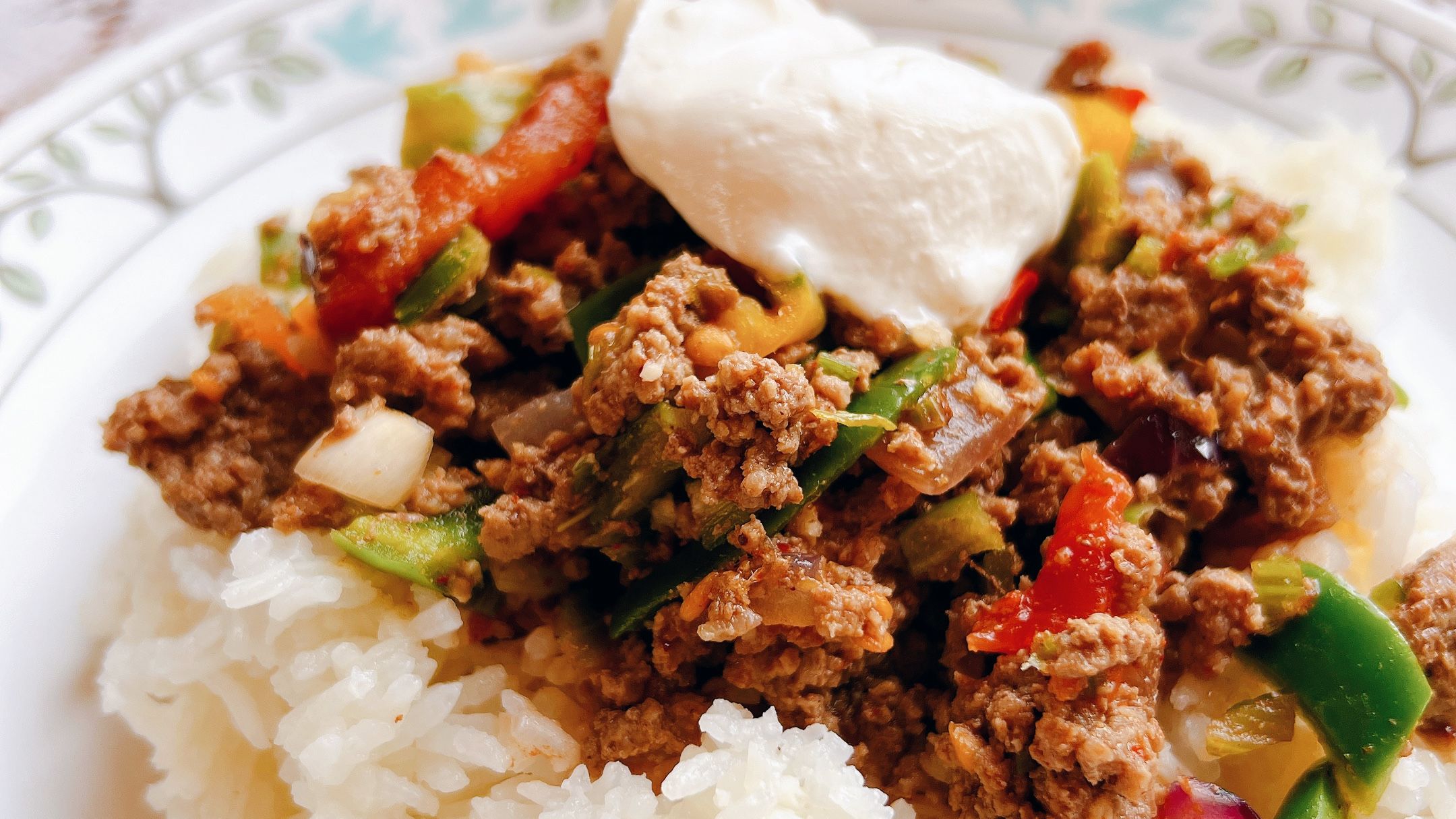 A mixture of hamburger, bean and vegetables on a plate of rice.