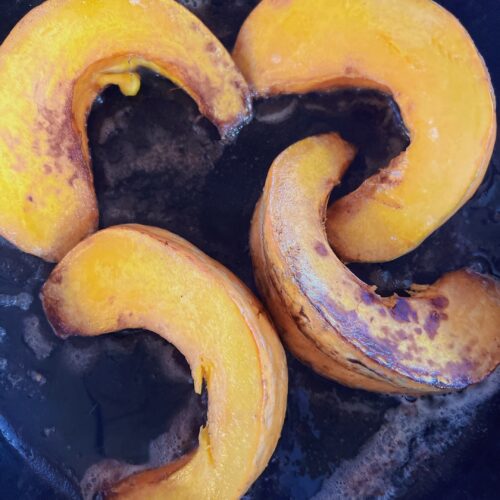 4 squash slices on a black plate that look candied.