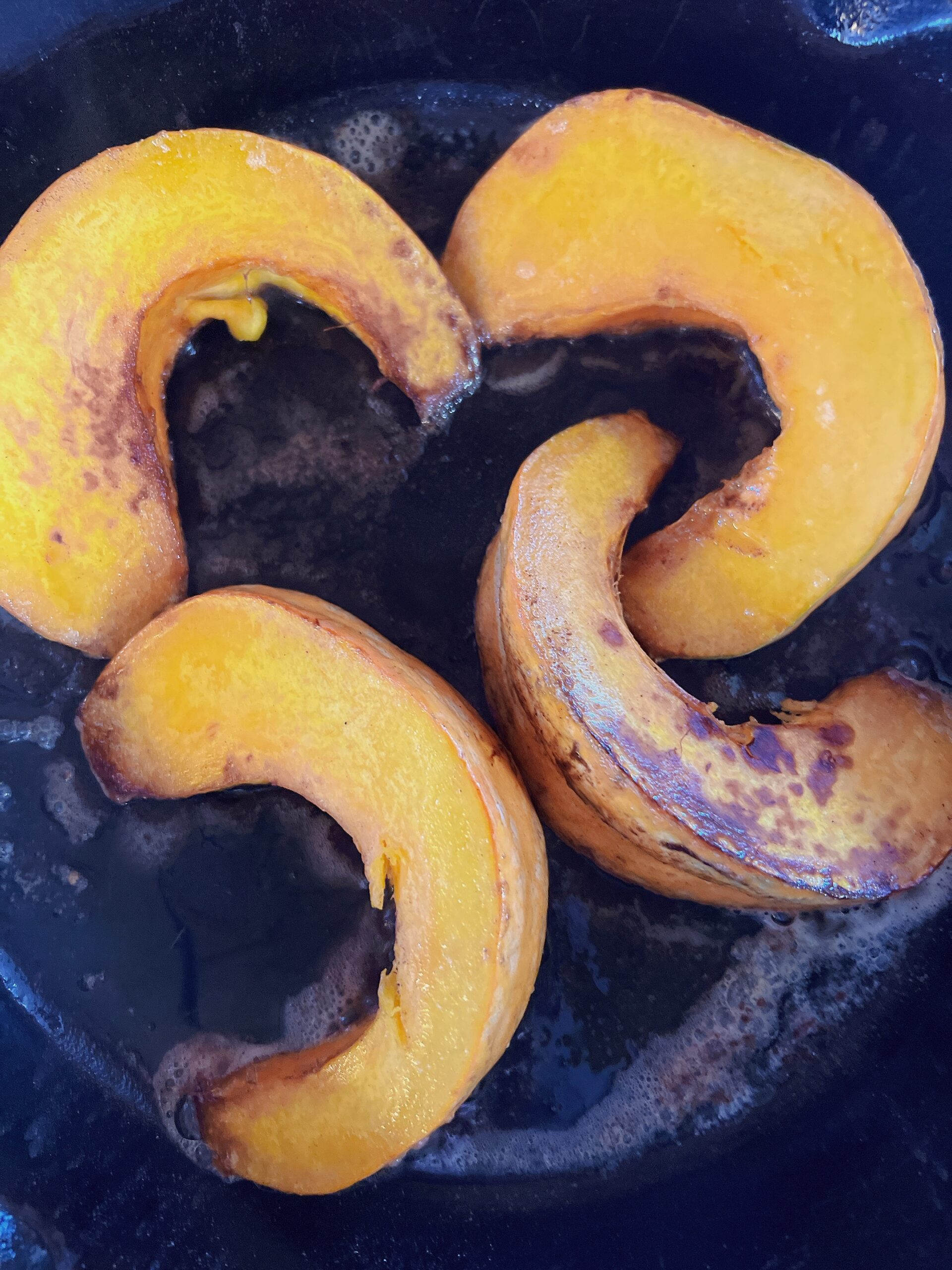 4 squash slices on a black plate that look candied.