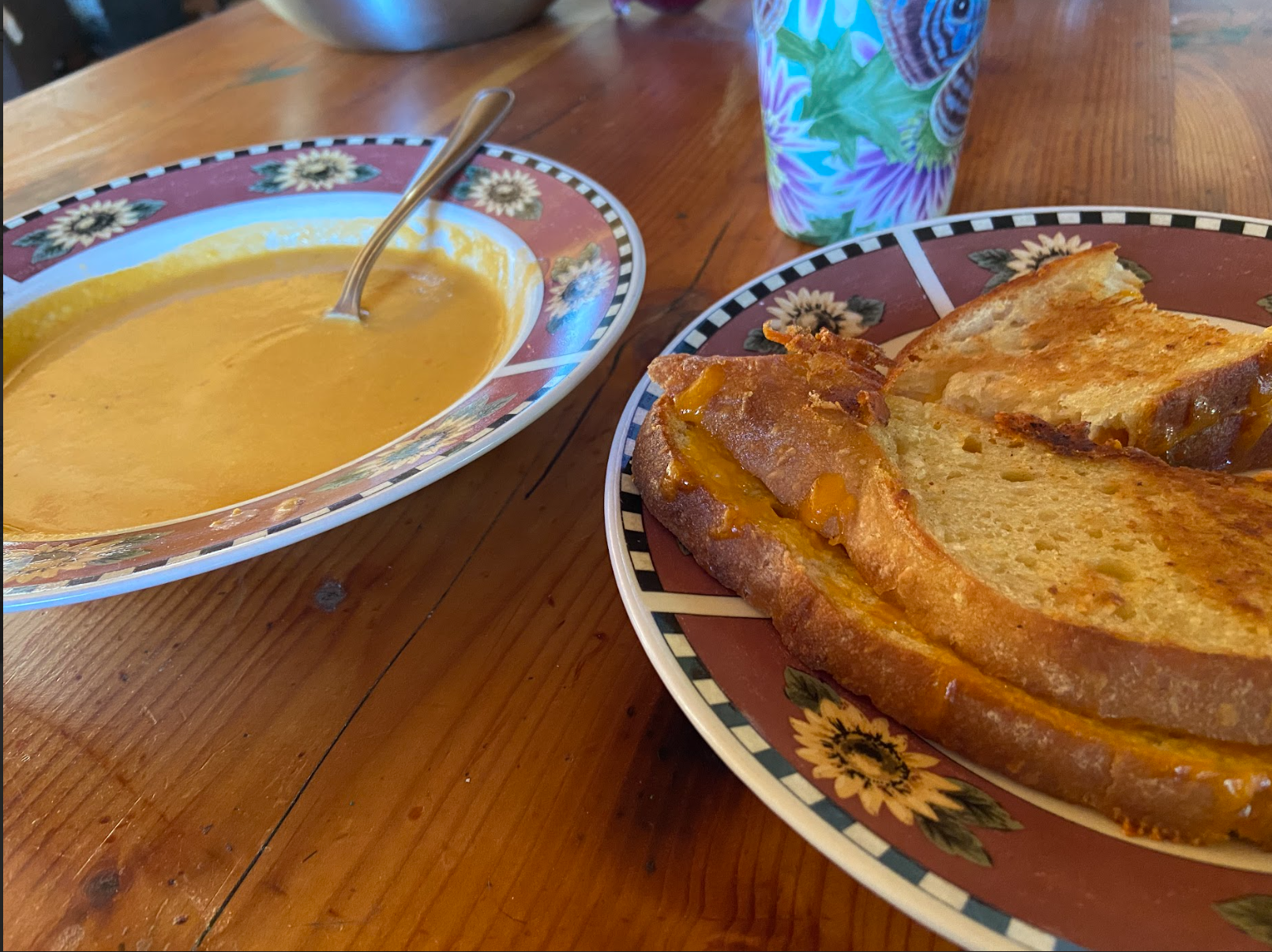 A bowl of yellow colored tomato soup and a plate of a grilled cheese sandwich.