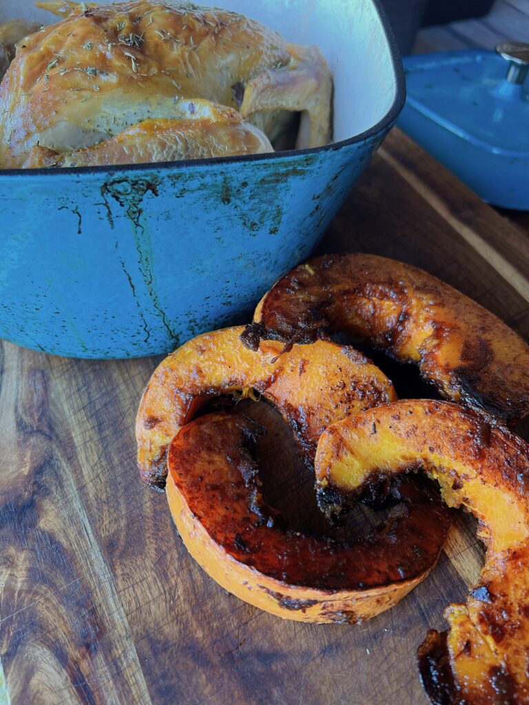 Candied squash slices on a wooded counter next to a blue pot of food.