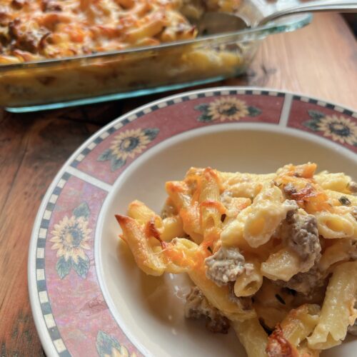 A white plate with a sunflower design that has a pile of sausage kale pasta with 20 minute creamy white sauce recipe on it.