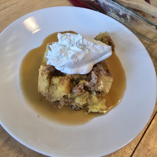 A white plate with pumpkin spice baked french toast casserole topped with whipped cream.