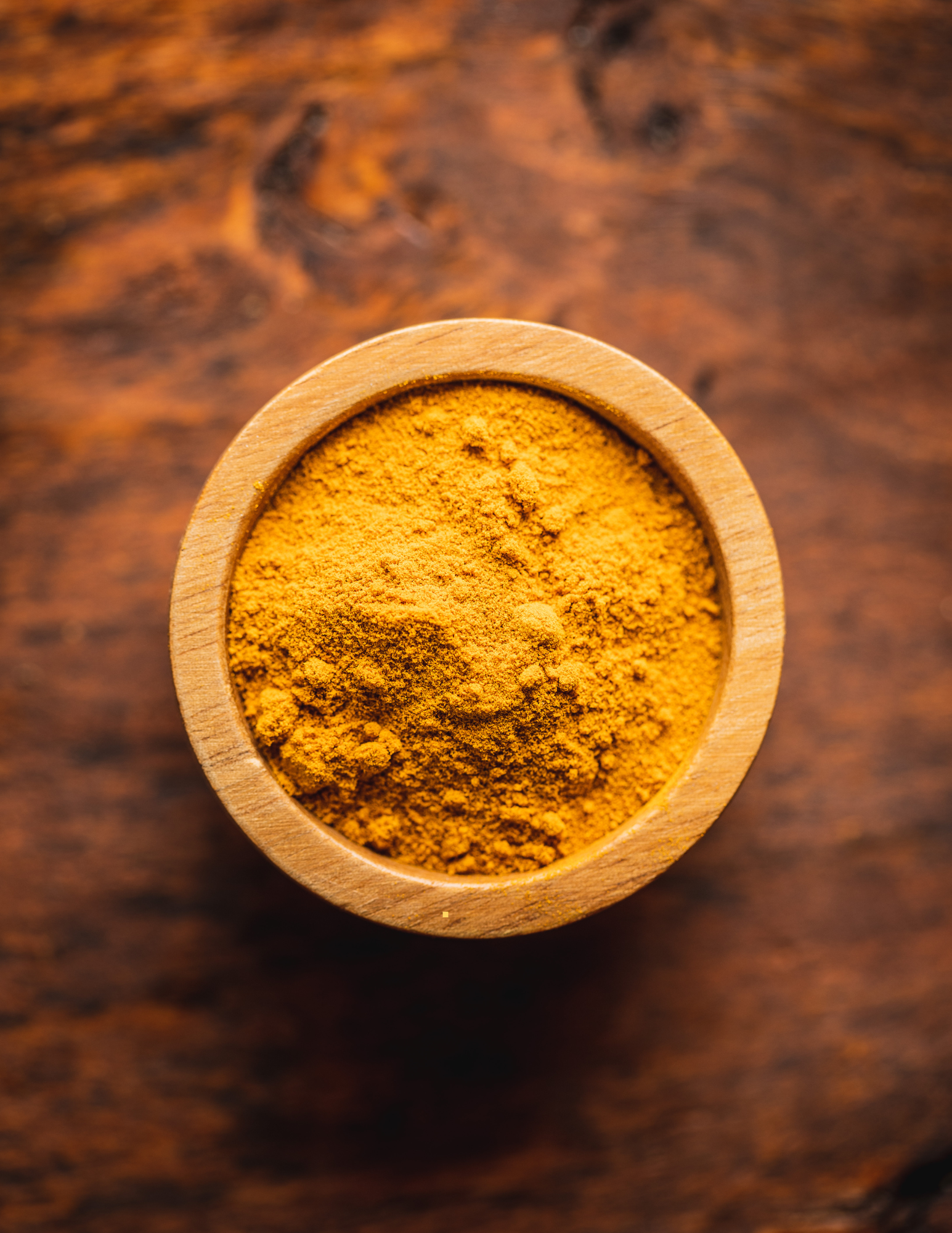 A wooden bowl tilled with homemade pumpkin pie spice on a wooden counter.