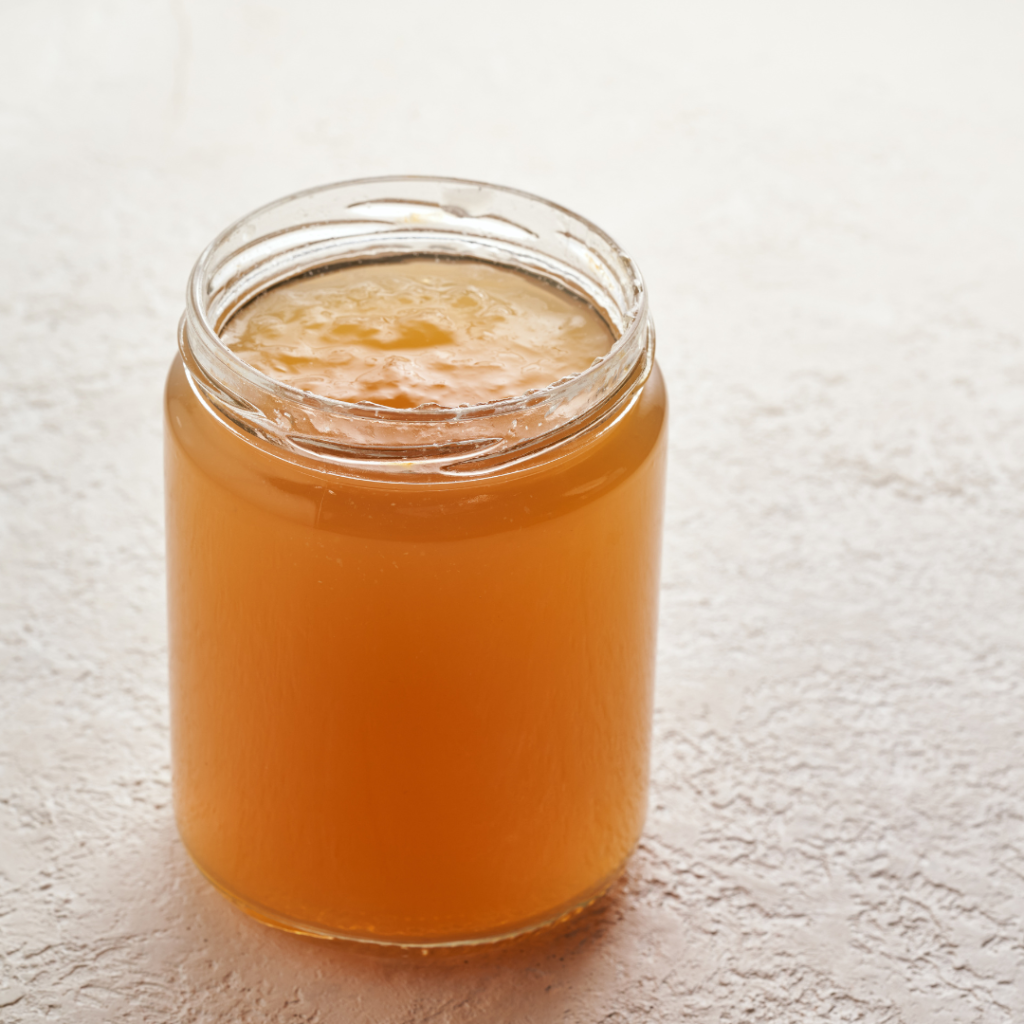 A plain mason jar filled with a dark yellow gelatin broth.