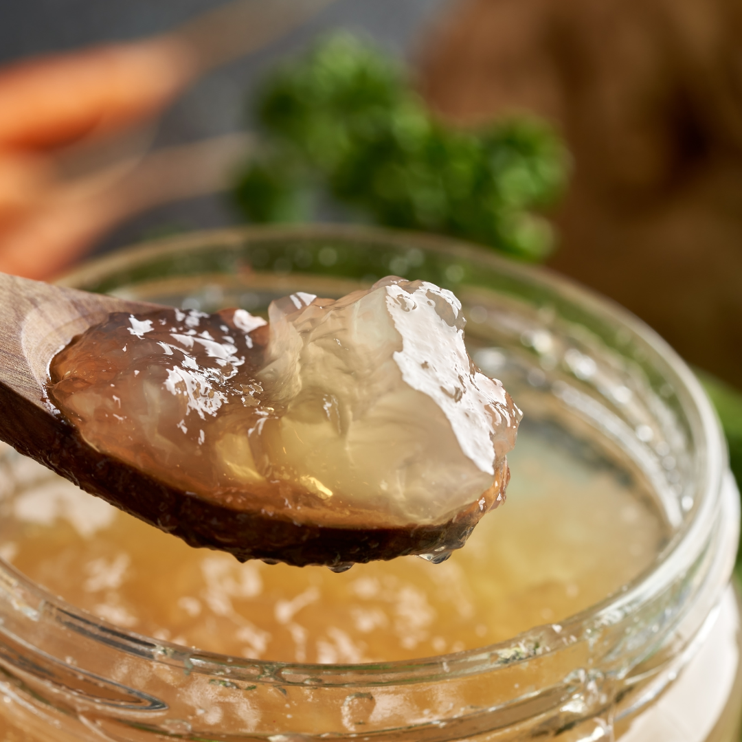 A mason jar with a spoon over top, both filled with gelatinous broth in it.