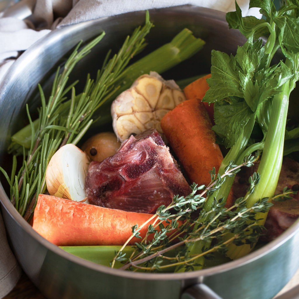 A stainless steel pot filled with meat bones and carious vegetables.