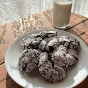 A white plate full of dark brown, powder coated round cookies and a glass of milk.