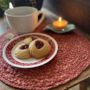 A white plate with a red rim that has three of Grandma's Raspberry Jam Thumbprint Cookies.