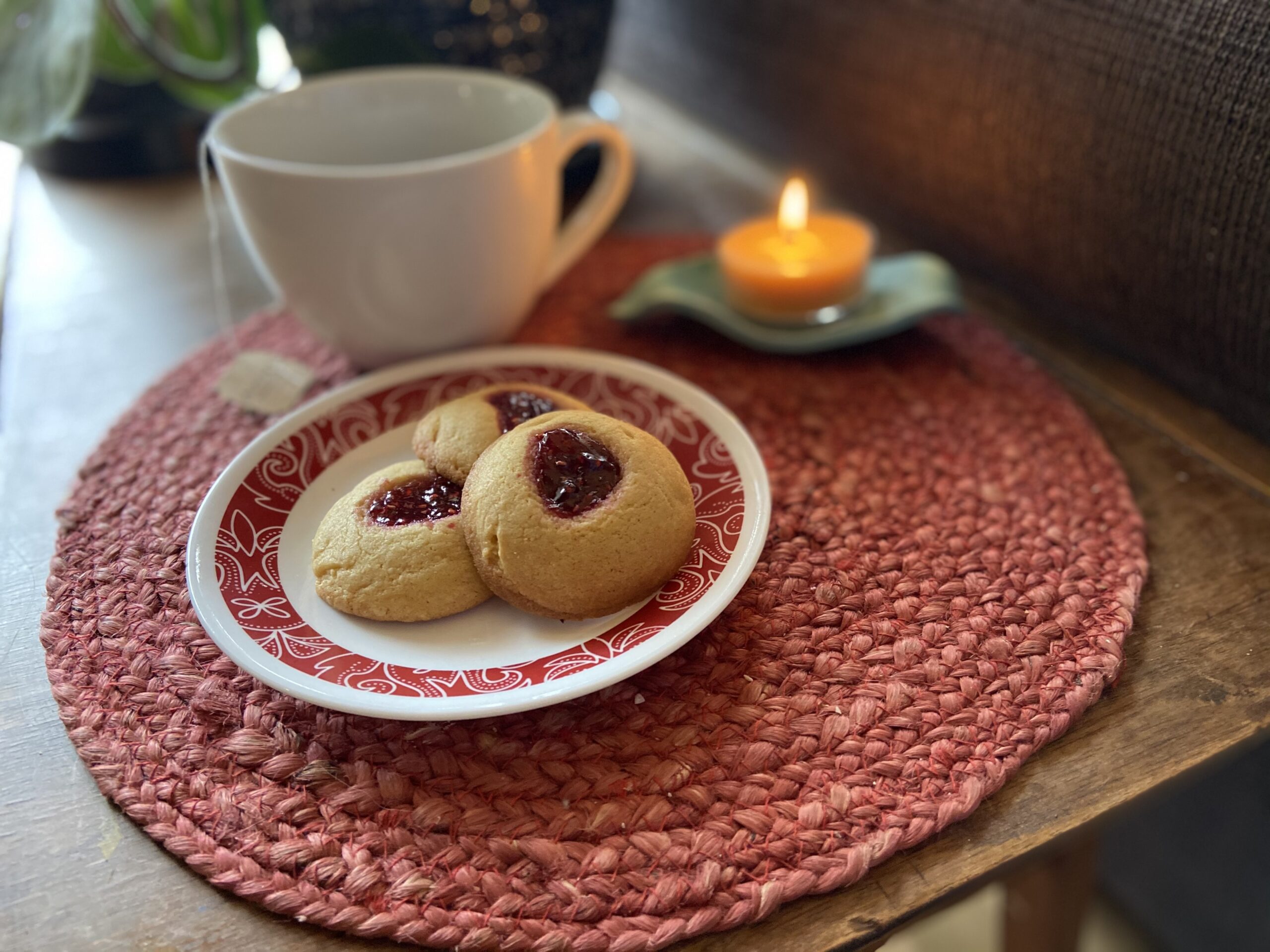 A white plate with a red rim that has three of Grandma's Raspberry Jam Thumbprint Cookies.