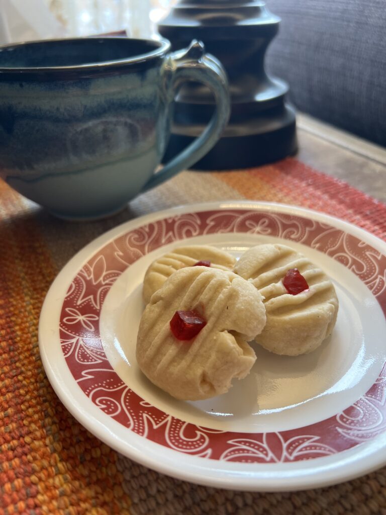 A white plate with red trim sitting on a wooden table with three shortbread cookies on it.