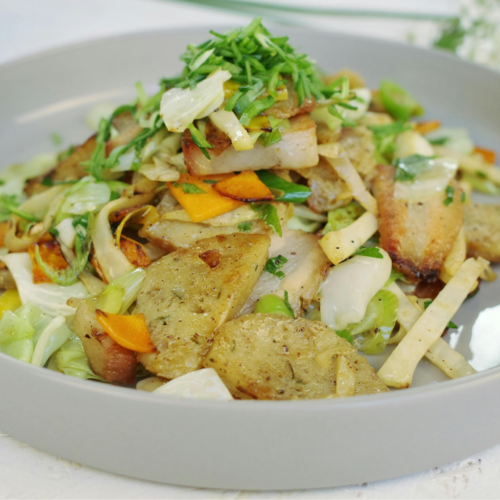 A shallow grey serving dish with stir fried cabbage and potatoes in it topped with green onions.