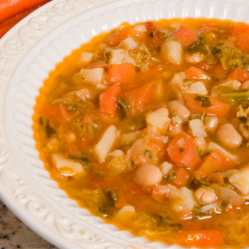 A white bowl of red lentil soup with raw carrots on next to it.