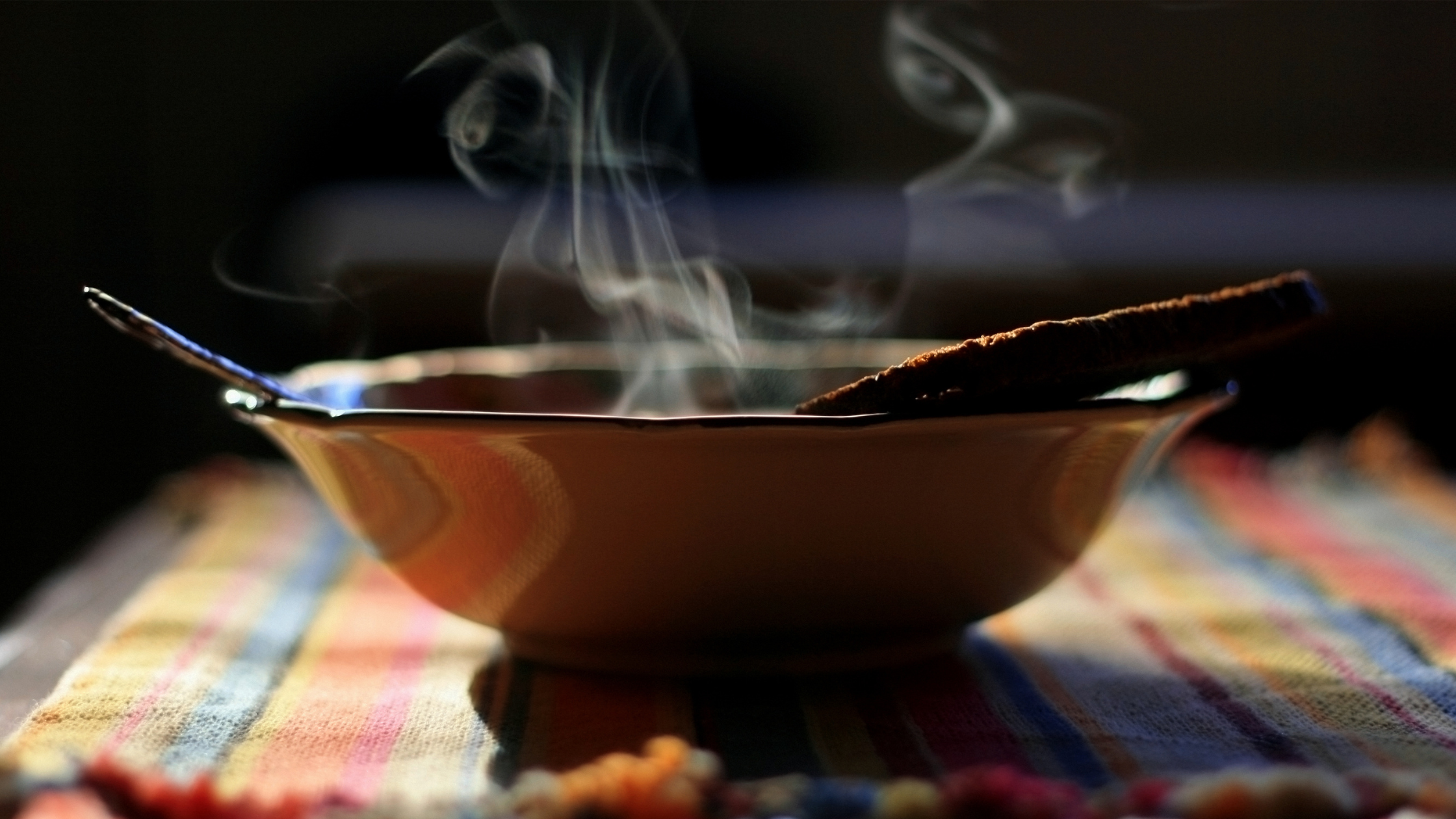 Close-up of a steaming bowl of homemade soup with a slice of bread resting on the rim, set on a colorful striped cloth