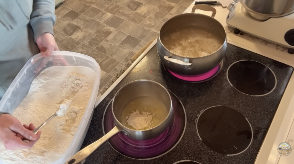 A pot on the stove as someone scoops flour into the pot to make a white sauce.