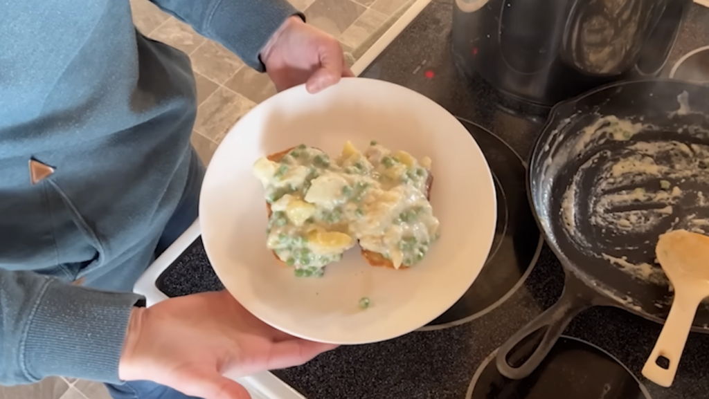 Chelsea holding a white plate with toast covered in a potatoes and peas white sauce.