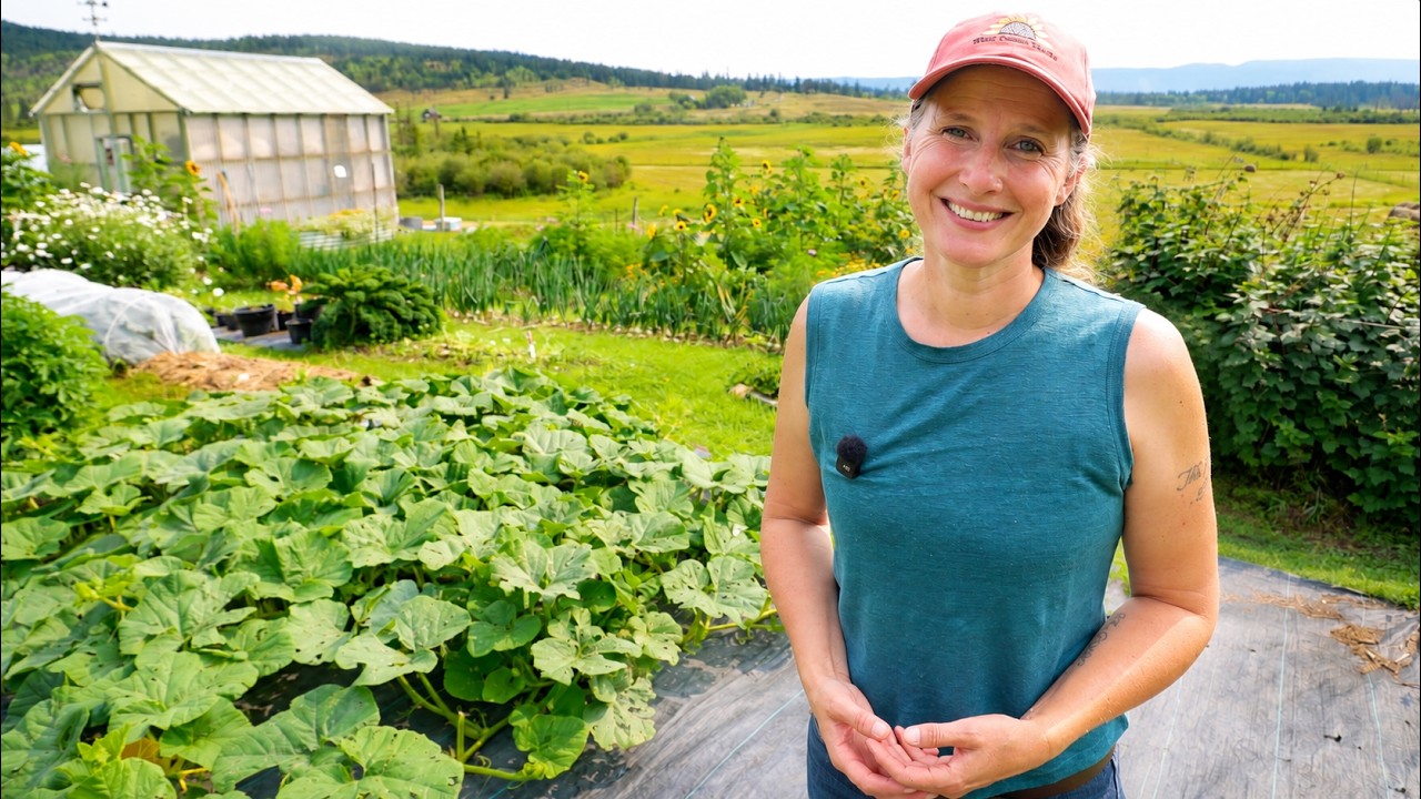 Chelsea wearing a teal shirt standing in front of her pumpkin patch and little greenhouse.